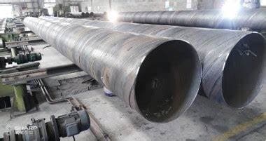 Se observan varios tubos helicoidales de gran diámetro dispuestos en un entorno industrial. La iluminación resalta su acabado metálico, y se pueden ver algunas maquinaria y estructuras en el fondo de la imagen.