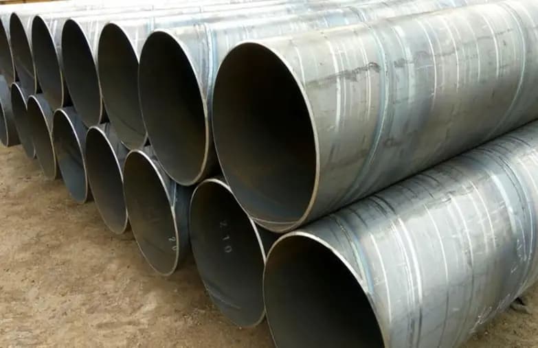 Se observan varios tubos helicoidales apilados, con un acabado metálico y superficie rayada. Están dispuestos de manera ordenada sobre un terreno de tierra.
